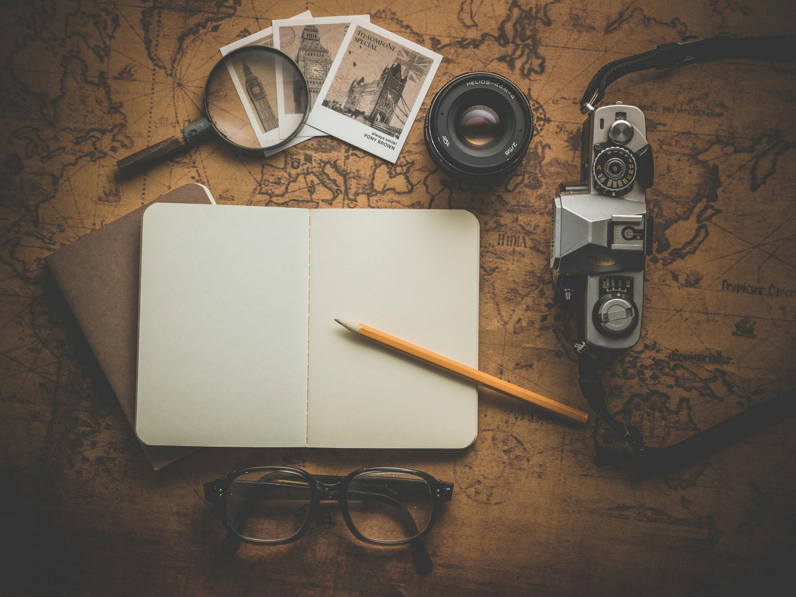 old-retro-antique-vintage-163185-163185 A flat lay of travel essentials on a vintage map surface, including a camera, notebook, and magnifying glass.