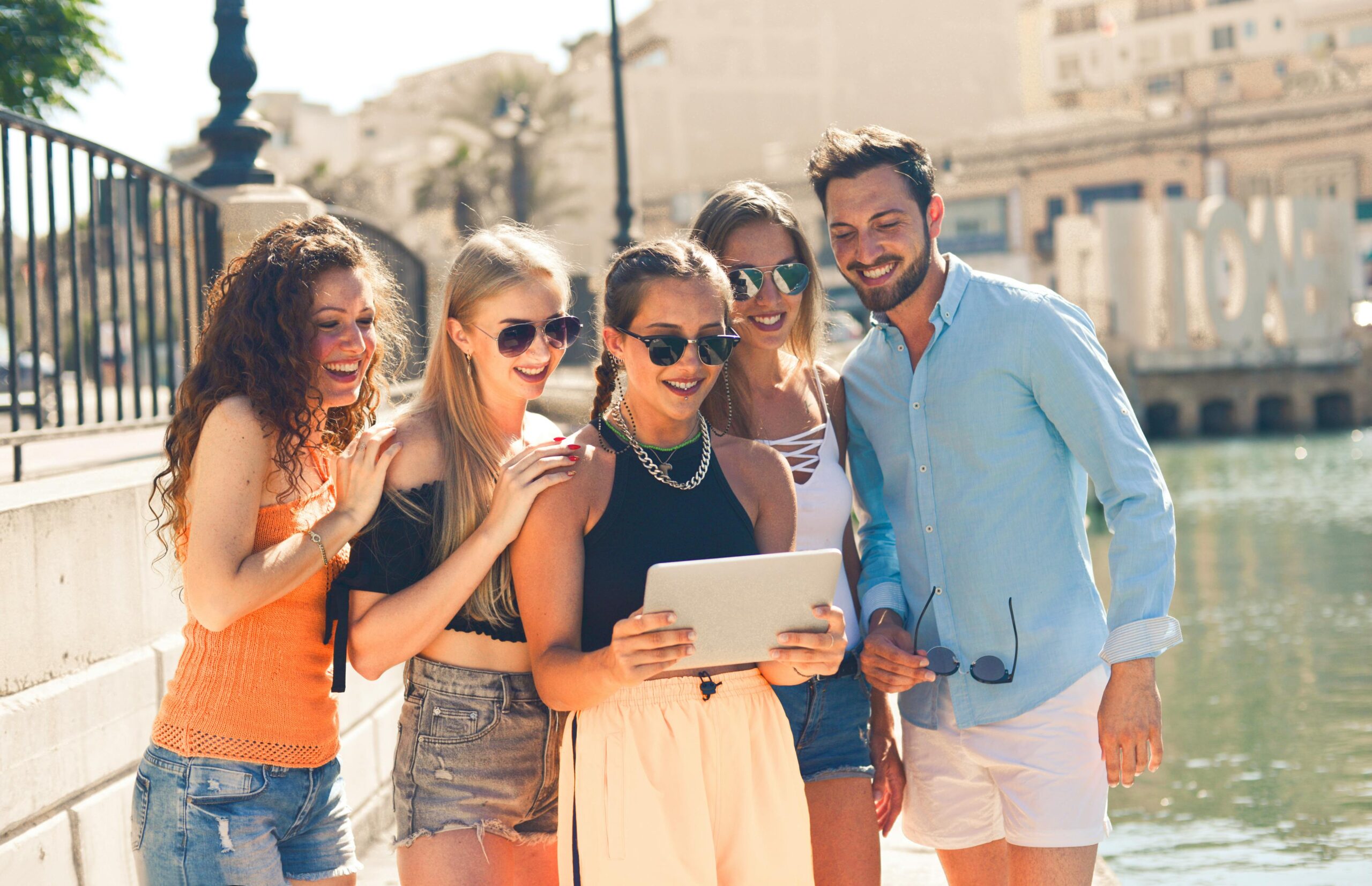 pexels-photo-2672979-2672979 Five friends laughing together by the waterfront in Malta, enjoying a sunny day and sharing a tablet.